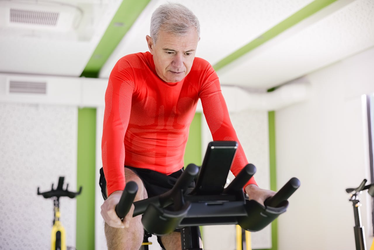 services-01 Senior man in red activewear exercising on stationary bike indoors, promoting healthy lifestyle.